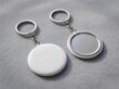 © Dadax - Two blank round keychains, one white and one metallic, on a grey textured surface, ready for customization.