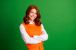 © deagreez - Smiling redhead woman in orange sweater vest with arms crossed against green background, confident casual portrait and friendly lifestyle concept