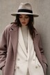 © YADigital - Elegant woman in chic beige fedora and oversized camel coat posing confidently against neutral urban wall, stylish autumn fashion with white double-breasted blazer and ribbed turtleneck, moody