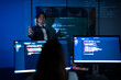 © Velocitystock777 - Smiling Asian male software developer gesturing during a presentation with programming code projected on a screen in a blue-lit room