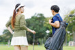 © Tj - Golfers discussing game strategy and course conditions, female player holding a club with a male caddy carrying a golf bag, enjoying a day of recreation and outdoor sport