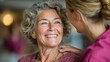 © COK House - A smiling elderly woman with gray hair looks at a younger woman in a pink top who is touching her shoulder against a blurred.