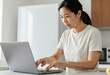 © Pixel-Shot - Remote work and digital nomad lifestyle, focused woman working on a laptop at home kitchen counter with deadline pressure and professional multitasking