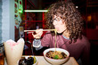 © Mediaphotos - Young adult Asian woman eating ramen noodles with chopsticks in Asian restaurant. Image represents food culture and is suitable for culinary blogs and restaurant marketing, close up shot