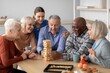 © Prostock-studio - Happy Group Of Senior Adults, Including Men And Women, Engaged In Playing Jenga Together At Home In A Living Room, Sharing Joyful Moments And Strengthening Family Bonds, Family Bonding Concept.
