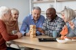 © Prostock-studio - Joyful Emotion. Happy Diverse Group Of Seniors Including Men And Women, Engaging In Jenga Game At Home Setting. They Are Enjoying Their Time Together, Smiling And Having Fun. Family Concept.