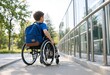 © shahjalal - Young child in wheelchair with blue backpack uses an accessible ramp outside a modern building, representing inclusion, mobility, independence, education, and accessibility.