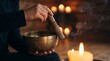 © Darakorn - Close up of hands playing a Tibetan singing bowl with a wooden mallet, surrounded by warm candle light and burning incense smoke during a sound therapy and meditation session.