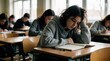 © miss irine - Teenage girl looking bored at desk in classroom. Students study and write in notebooks during lesson. Quiet learning environment. Others concentrate on work.