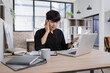 © SOMKID - A young Asian businessman talking on a mobile phone while taking notes and working on a laptop at his office desk.