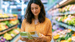 © Yuwarin - a young woman standing in a modern supermarket comparing two generic food packages with blank labels, carefully choosing the healthier option, healthy grocery shopping, wellness lifestyle