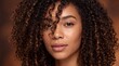 © Curioso.Photography - Woman with curly hair posing confidently against a warm brown background.
