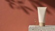 © Aboubakar - Blank cosmetic squeeze tube mockup on concrete pedestal with terracotta background and leaf shadow
