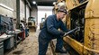 © Shara - Professional mechanic repairing a large yellow industrial tractor engine inside a busy mechanical workshop garage