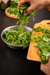 © Inna Nikitina - Chef hands cooking fresh green sorrel leaves close up. Putting chopped organic spinach or herbs into metal bowl. Vertical rustic kitchen food photography with human interaction