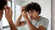 © Maryna - Young man with curly hair styles it in a modern bathroom mirror. He adjusts his hairstyle with his fingers, getting ready for his day with clean grooming.