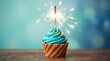 © Huzayfa - A beautifully decorated turquoise frosted cupcake is shown with a single bright sparkler lit on top against a softly blurred teal background