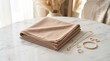 © zalfa_std98 - Folded beige fabric napkin with gold jewelry on marble table.