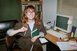 © AnnaStills - Portrait of smiling young adult Caucasian woman sitting at desk in retro office holding notebook and pencil. Image represents vintage corporate style, suitable for nostalgic business marketing