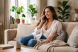 © JuanM - Young woman talking on phone sitting on cozy sofa at home