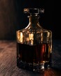 © Aleksey - Elegant glass whiskey decanter with dark amber spirit on a wooden surface, illuminated by warm dramatic light for a refined moody autumn bar atmosphere.