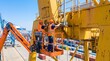 © Resfa - Two workers in hard hats and safety vests repairing yellow port crane from aerial work platform. Industrial maintenance at container terminal. Heavy machinery service and logistics operations concept.