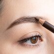 © Pravinrus - Macro shot of a young woman shaping and filling her eyebrows with a brown cosmetic pencil, highlighting natural beauty, skincare, and daily makeup routine details.