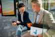 © Davor - Colleagues discussing work over coffee at a city bus stop