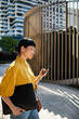 © Davor - Businesswoman using smartphone while walking downtown with laptop