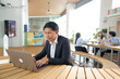 © blueringmedia - Asian Businessman Working on Laptop in Modern Outdoor Coworking Space