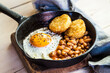 © Westend61 - Fried egg, baked beans and hash browns in frying pan on wooden board