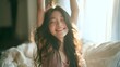 © Yassine - Young asian woman stretching arms happily while waking up in her cozy bright sunlit bedroom during a relaxing morning time