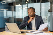 © Liubomir - Experienced entrepreneur focusing on analyzing business documents while using a laptop at an executive desk, planning financial strategies and making important decisions