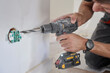 © barmaleeva - Man drills into wall beside exposed electrical outlet and wiring