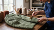 © primipil - Senior Woman Cleaning Green Knitted Sweater with Special Fabric Brush at Wooden Workshop Table. Concept of wool care, clothes maintenance, sweater comb, pilling removal, garment care.