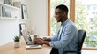© mdtuhin - Smiling Black man working on laptop in bright home office, remote professional at desk