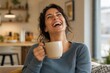 © Andrii Prokhorov - Woman with dark hair in blue sweater laughing while holding a beige mug in a cozy living room with plants and a kitchen visible in the background, creating a warm and inviting atmosphere