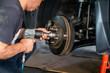 © Koonsiri - Selective focus to professional mechanic using a pneumatic impact wrench to service the brake disc assembly and wheel hub of a car supported by a jack stand in a repair shop.