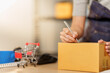 © Natee Meepian - Cropped hands writing address on cardboard parcel box for small business delivery