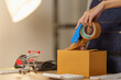 © Natee Meepian - Cropped hands taping cardboard box with tape dispenser for e-commerce order shipping