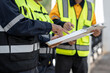 © Thitaporn - Construction workers in high visibility safety vests review documents on a clipboard during an on-site inspection and project meeting.