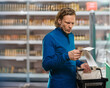 © Denys Kurbatov - Man inspecting grocery receipt in store, budget conscious shopper reviewing multiple receipts, comparing prices and discounts, showing surprise and concern, reusable tote on arm,