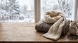 © MstRowshanara - Cozy winter scene with knitted scarf and sweater on wooden table by snowy window