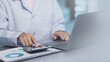 © Antony Weerut - Doctor using calculator to analyze healthcare business data, representing medical growth investment, health insurance cost estimation, financial report, medical business, healthcare budget planning.