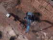 © Amazing Aerial - Aerial view of a blue forestry machine loading logs onto a truck at a timber yard in Gdansk, Poland.