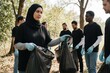 © Pete - Muslim woman with headscarf leads diverse volunteers in forest cleanup. Team collects trash in bags for eco conservation. Community effort promotes environmental responsibility and social action.