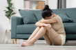 © Thitiporn - Stress and emotional health concept showing a tired woman sitting on the floor holding her glasses with head down at home. stress, fatigue, anxiety, burnout, mental health