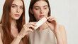 © jockermax3d - Two young women holding a white and pink cosmetic bottle in a studio
