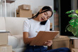 © David - Young woman managing home based business, multitasking with phone call and writing on clipboard, surrounded by shipping boxes for e commerce startup operations