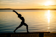 © Metadancer - Hispanic woman performing yoga stretch pose by lake at sunset in USA